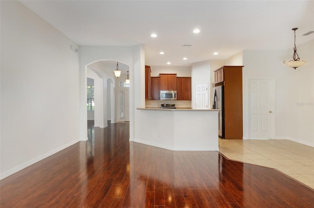 kitchen with decorative light fixtures, dark hardwood / wood-style floors, kitchen peninsula, and appliances with stainless steel finishes