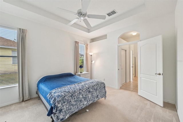 bedroom featuring ceiling fan, light colored carpet, and a tray ceiling