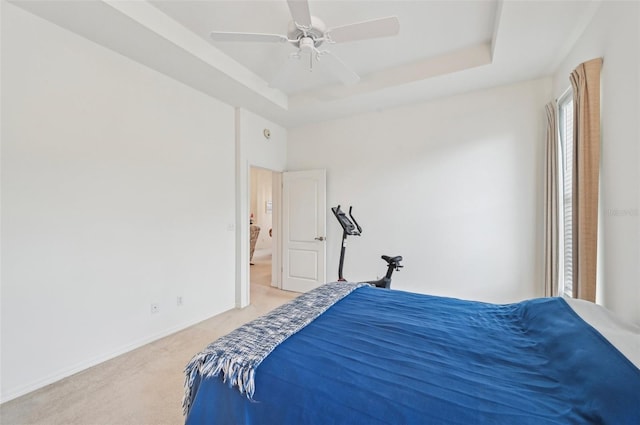 bedroom featuring ceiling fan, ensuite bathroom, light colored carpet, and a tray ceiling