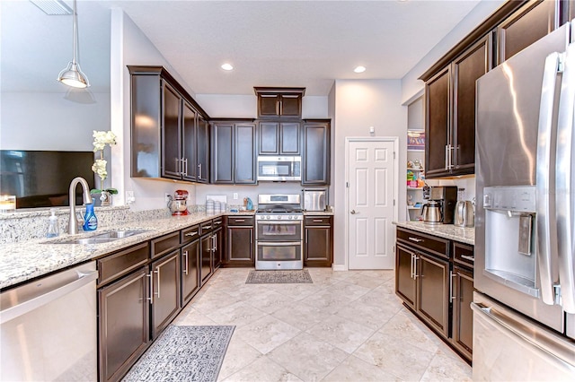 kitchen with pendant lighting, sink, stainless steel appliances, light stone counters, and dark brown cabinetry