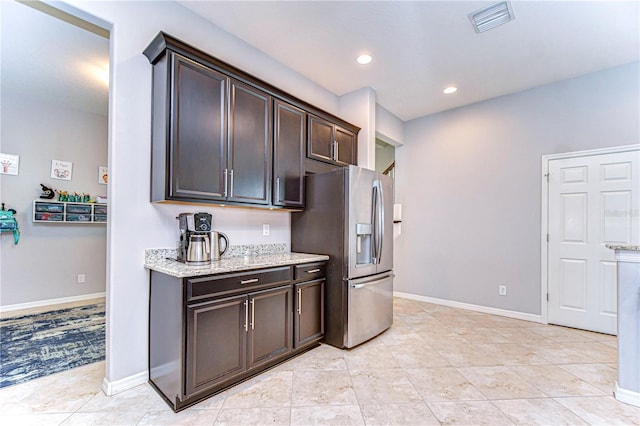 kitchen featuring light stone countertops, light tile patterned floors, stainless steel fridge, and dark brown cabinetry