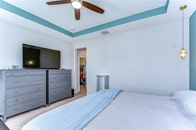 carpeted bedroom with a walk in closet, a textured ceiling, a tray ceiling, a closet, and ceiling fan