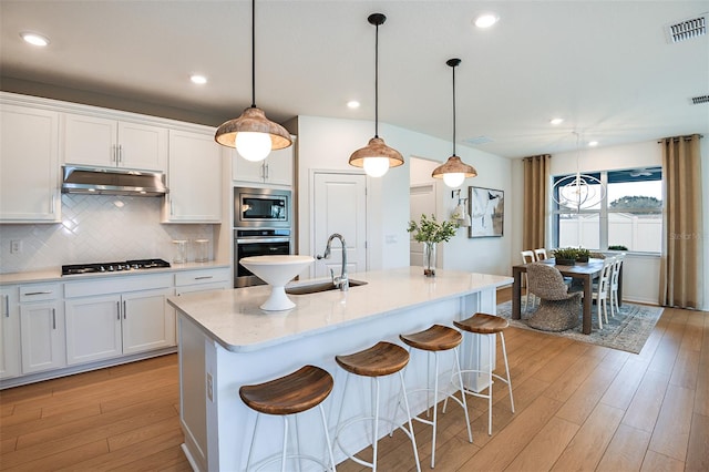 kitchen with white cabinetry, appliances with stainless steel finishes, sink, and a center island with sink