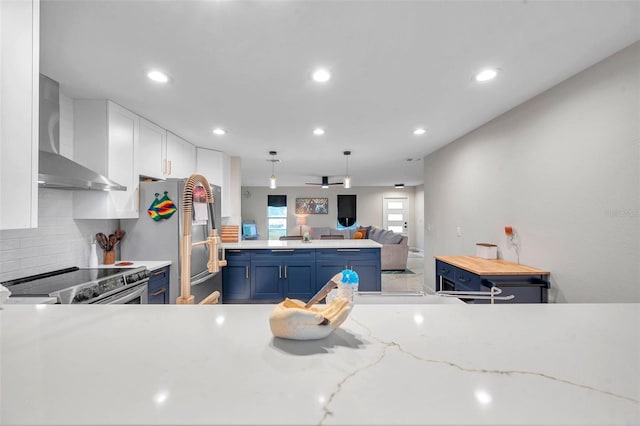 kitchen with blue cabinetry, appliances with stainless steel finishes, backsplash, white cabinets, and wall chimney exhaust hood