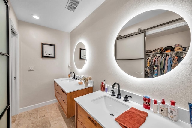 full bath featuring two vanities, visible vents, a sink, and baseboards