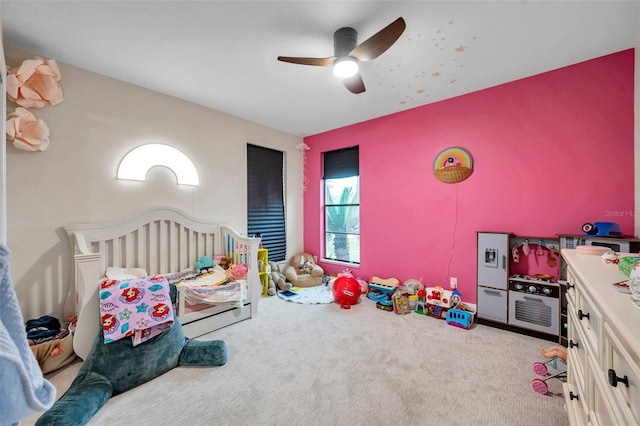 bedroom featuring a nursery area, light colored carpet, and ceiling fan