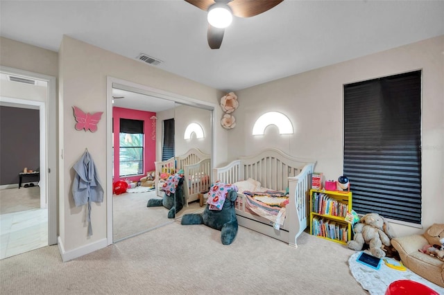 carpeted bedroom featuring a crib, ceiling fan, and a closet