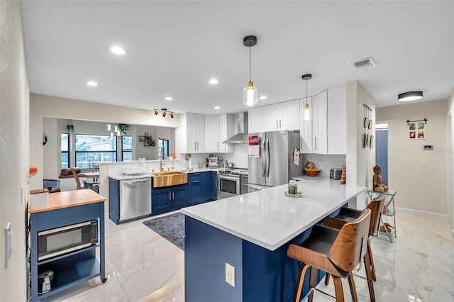 kitchen with marble finish floor, appliances with stainless steel finishes, blue cabinets, a peninsula, and wall chimney exhaust hood