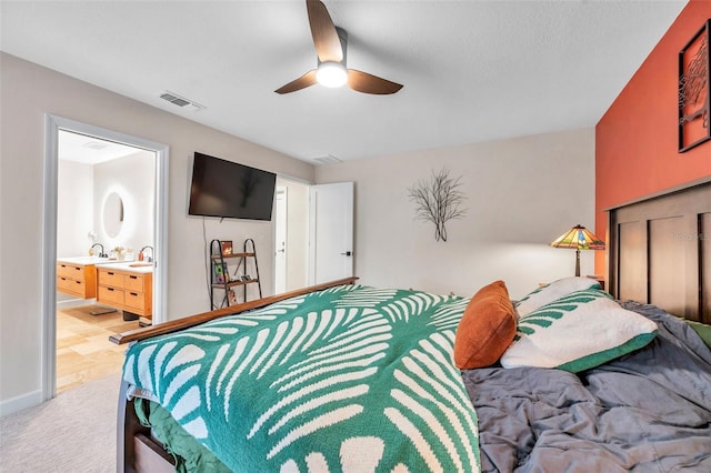 bedroom with light colored carpet, a sink, a ceiling fan, visible vents, and ensuite bath