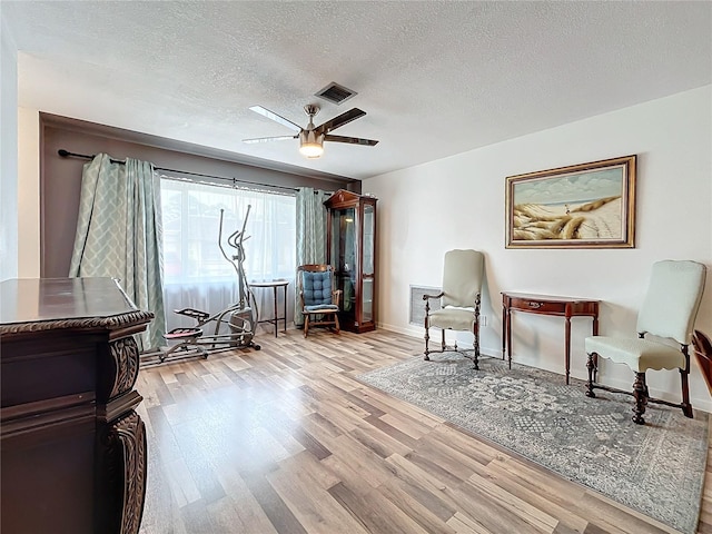 sitting room with ceiling fan, light hardwood / wood-style floors, and a textured ceiling