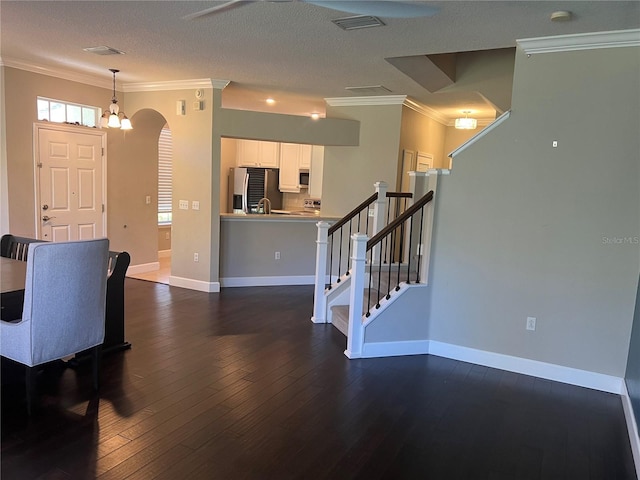 interior space with dark hardwood / wood-style floors, white cabinets, hanging light fixtures, stainless steel appliances, and crown molding