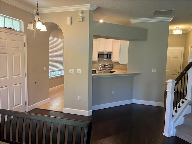 interior space featuring white cabinetry, crown molding, decorative light fixtures, and appliances with stainless steel finishes