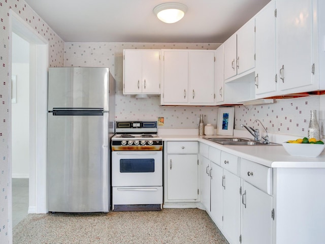 kitchen with gas range gas stove, white cabinetry, decorative backsplash, sink, and stainless steel refrigerator