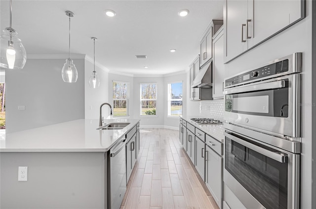 kitchen featuring appliances with stainless steel finishes, tasteful backsplash, sink, hanging light fixtures, and a center island with sink