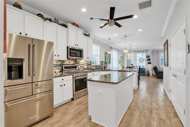 kitchen with white cabinets, appliances with stainless steel finishes, decorative light fixtures, and dark stone countertops