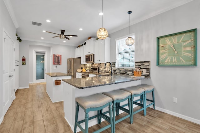 kitchen featuring a breakfast bar area, white cabinets, premium appliances, hanging light fixtures, and kitchen peninsula