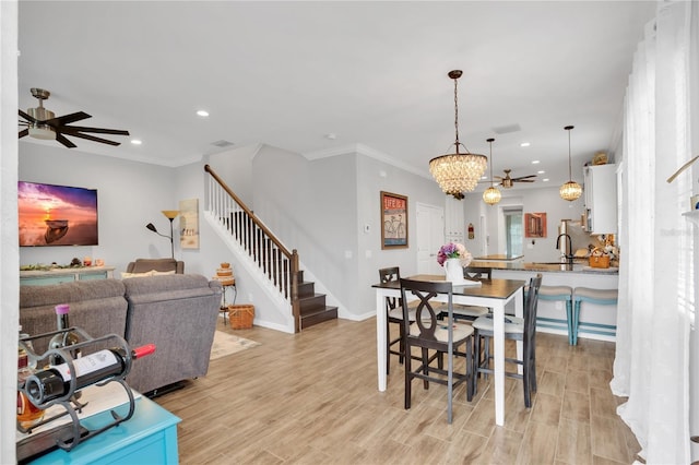 dining room with ceiling fan with notable chandelier, ornamental molding, sink, and light hardwood / wood-style flooring