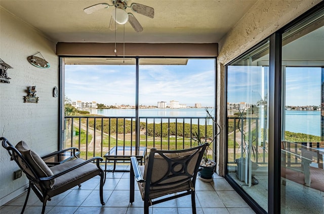 sunroom with ceiling fan and a water view