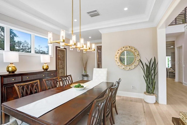 dining space featuring a tray ceiling, a notable chandelier, crown molding, and light hardwood / wood-style floors