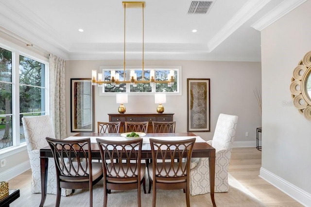 dining room with crown molding, a notable chandelier, a raised ceiling, and light wood-type flooring