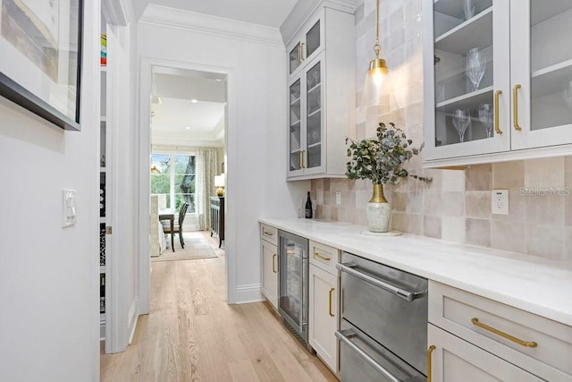 kitchen featuring pendant lighting, beverage cooler, decorative backsplash, ornamental molding, and light hardwood / wood-style flooring