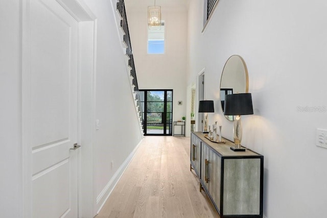 hallway featuring a chandelier, a high ceiling, and light wood-type flooring