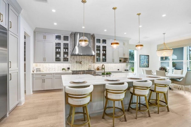 kitchen with pendant lighting, a large island, a breakfast bar area, light hardwood / wood-style floors, and wall chimney exhaust hood