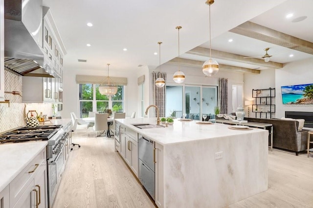 kitchen featuring white cabinets, decorative light fixtures, a large island with sink, and wall chimney range hood