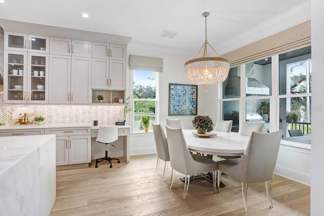 dining room with an inviting chandelier, ornamental molding, built in desk, and light hardwood / wood-style floors