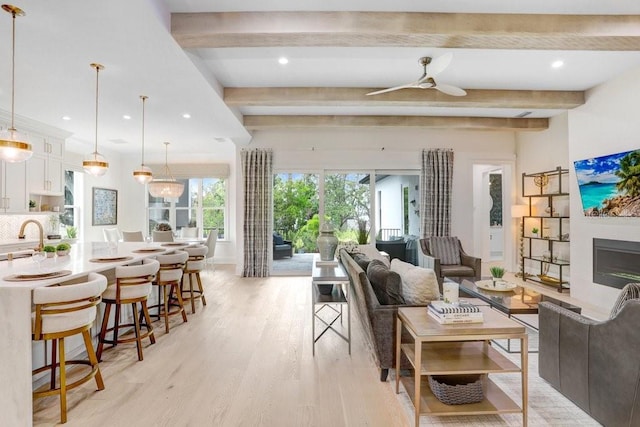 living room featuring sink, beam ceiling, light hardwood / wood-style flooring, and ceiling fan