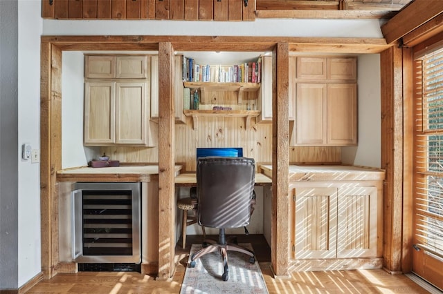 office area featuring wine cooler, light wood-type flooring, built in desk, and plenty of natural light