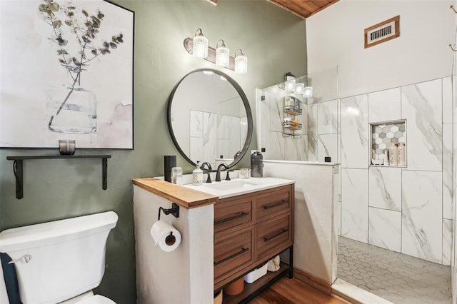 bathroom featuring a tile shower, vanity, hardwood / wood-style floors, and toilet