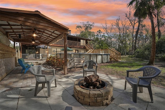 patio terrace at dusk featuring a gazebo, ceiling fan, and an outdoor fire pit