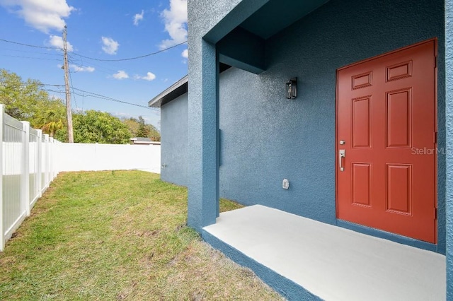 view of exterior entry featuring a patio and a lawn