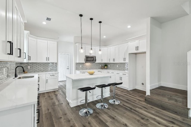 kitchen featuring sink, a center island, hanging light fixtures, decorative backsplash, and white cabinets