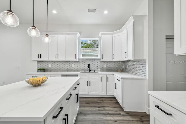 kitchen with decorative light fixtures, white cabinetry, sink, backsplash, and light stone counters