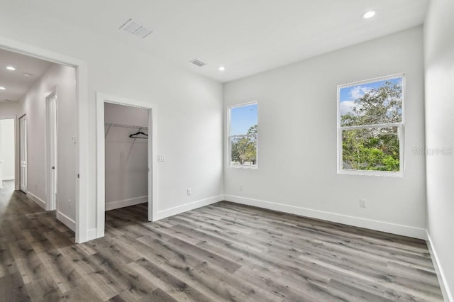 unfurnished bedroom with a closet, a spacious closet, and dark hardwood / wood-style floors