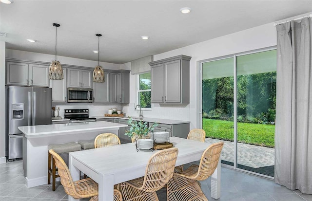 kitchen with a center island, appliances with stainless steel finishes, gray cabinets, pendant lighting, and decorative backsplash