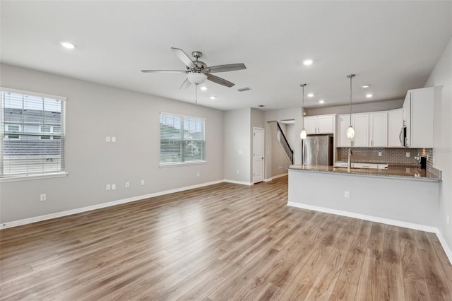 kitchen featuring white cabinetry, light stone counters, decorative light fixtures, plenty of natural light, and stainless steel fridge