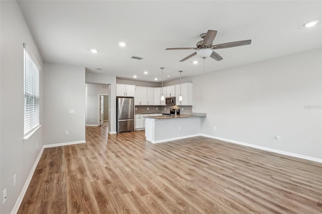 kitchen with hanging light fixtures, stainless steel appliances, tasteful backsplash, white cabinets, and kitchen peninsula