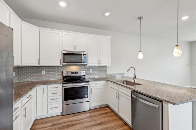 kitchen with appliances with stainless steel finishes, kitchen peninsula, sink, and white cabinets