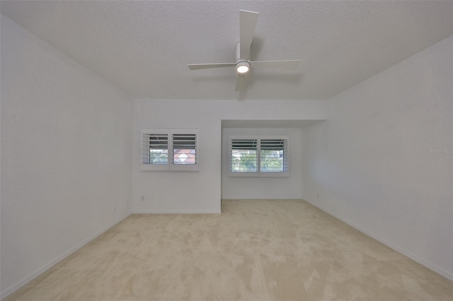 spare room with a textured ceiling, light colored carpet, and ceiling fan