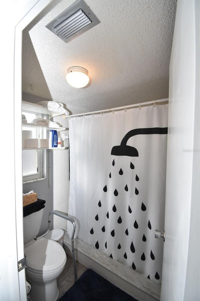 bathroom with a textured ceiling, toilet, and a shower with shower curtain