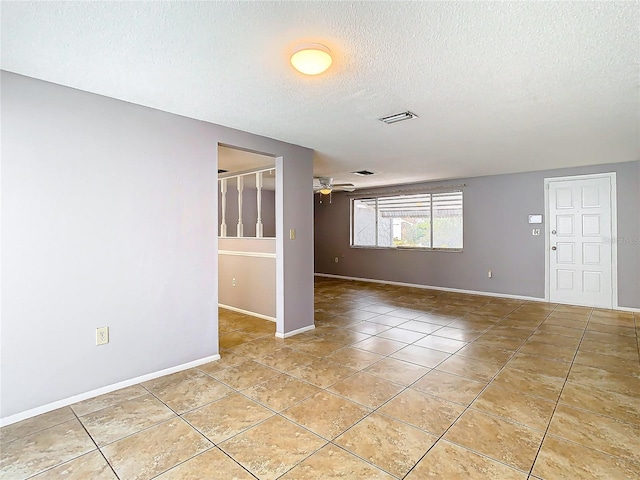 empty room with ceiling fan, a textured ceiling, and light tile patterned floors