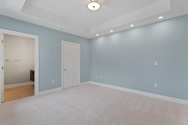 unfurnished bedroom featuring a raised ceiling, recessed lighting, carpet, and baseboards