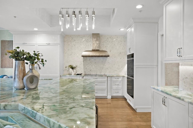 kitchen featuring pendant lighting, white cabinetry, decorative backsplash, light stone counters, and wall chimney range hood