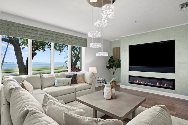 living room featuring visible vents, wood finished floors, an inviting chandelier, a fireplace, and crown molding