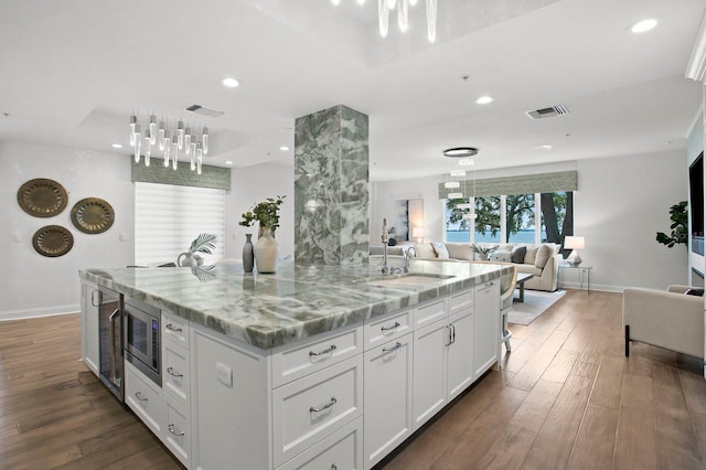 kitchen featuring stainless steel microwave, white cabinetry, an island with sink, sink, and light stone countertops