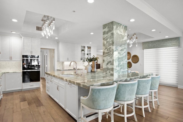 kitchen featuring a kitchen bar, light wood-style flooring, a raised ceiling, and a sink