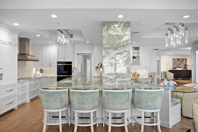 kitchen featuring white cabinetry, wall chimney exhaust hood, a raised ceiling, and backsplash